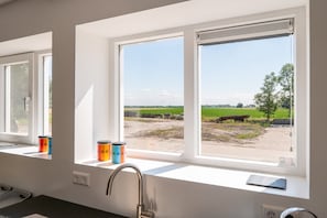 Une cuisine avec une fenêtre donnant sur un paysage rural, un évier et deux récipients posés sur le rebord de la fenêtre.