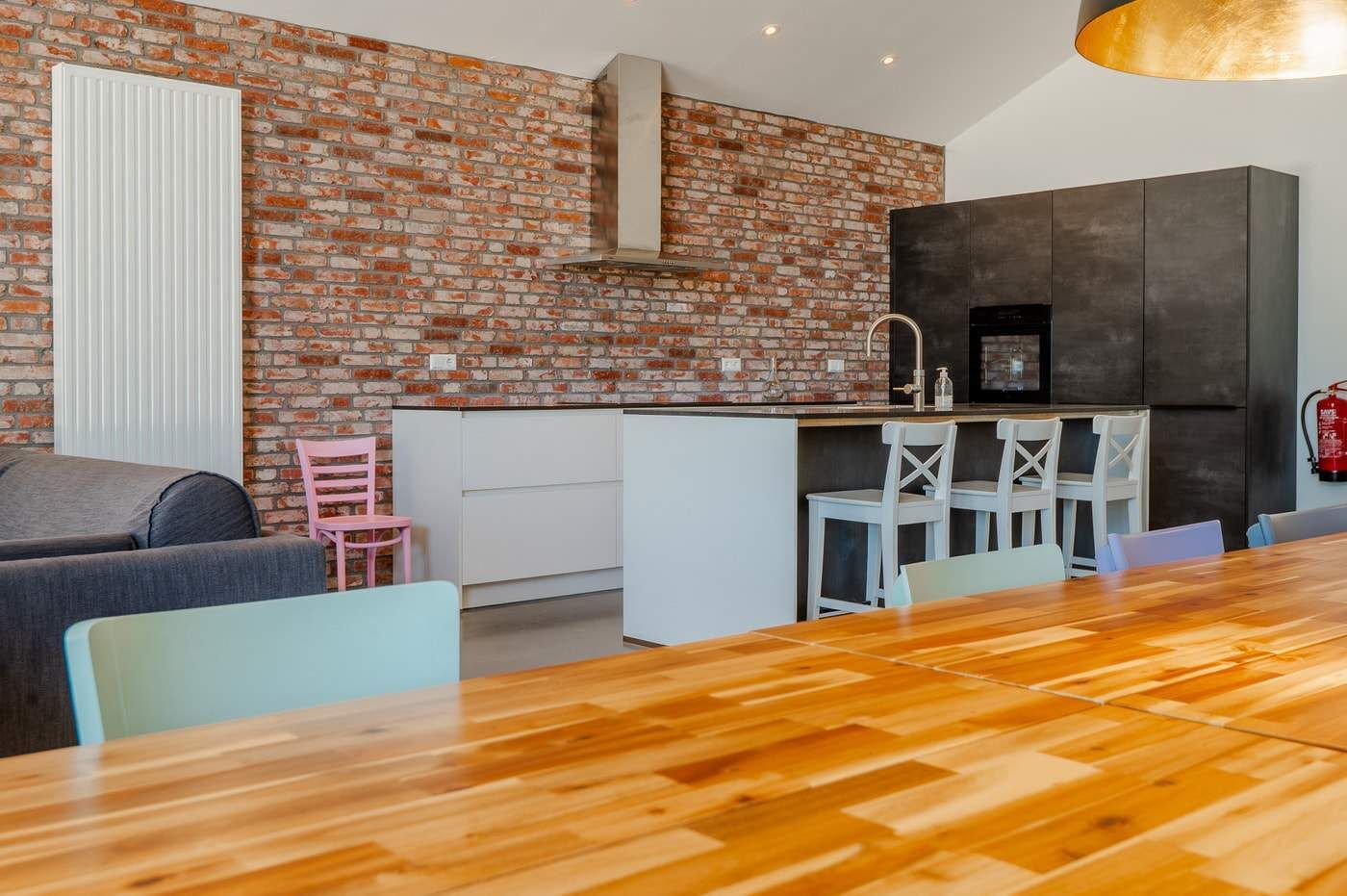 A modern kitchen with a brick wall, white cabinetry, and a wooden dining table.
