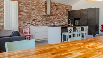 A modern kitchen with a brick wall, white cabinetry, and a wooden dining table.