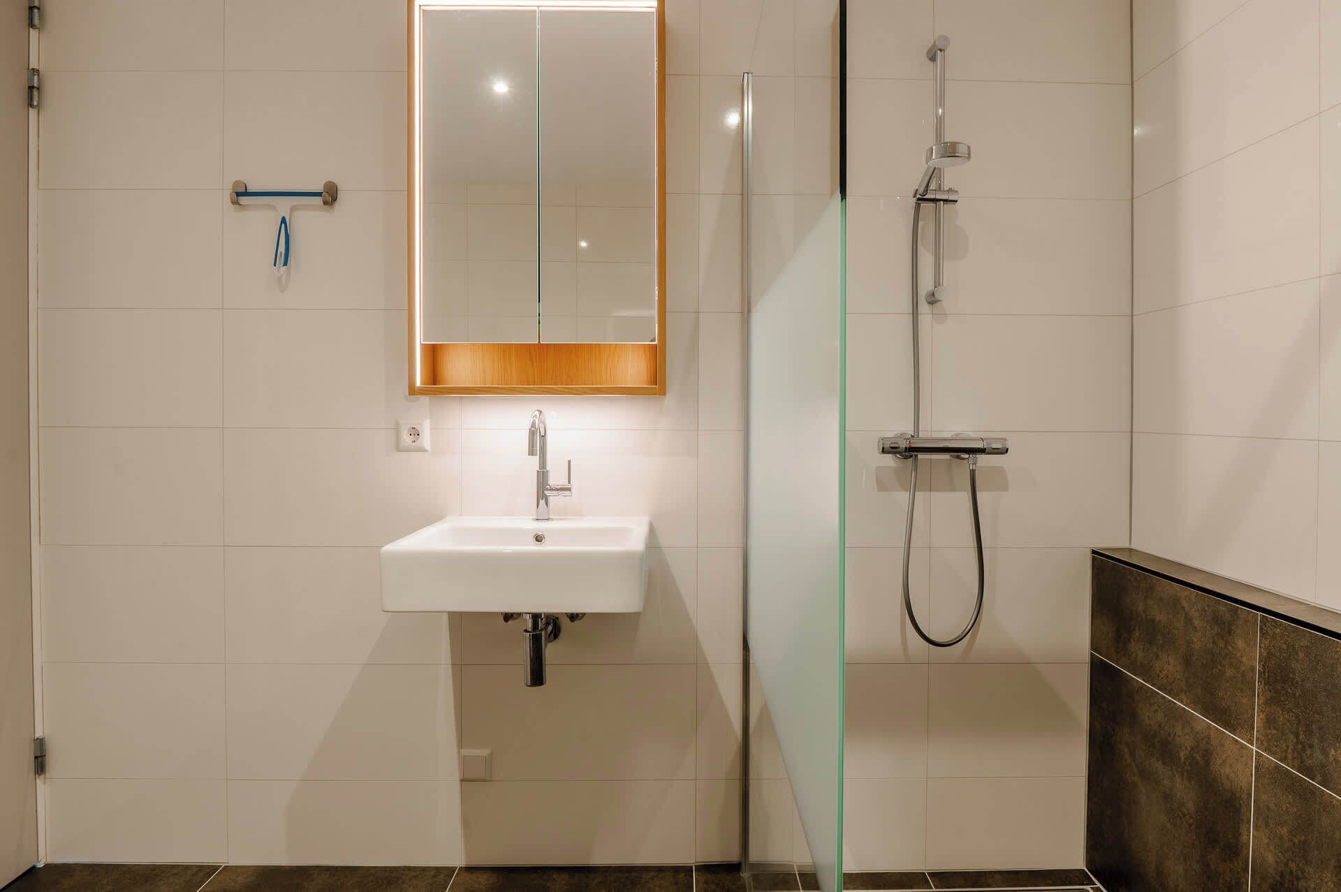 A modern bathroom with a white sink, a glass shower enclosure, and a wooden-framed mirror.