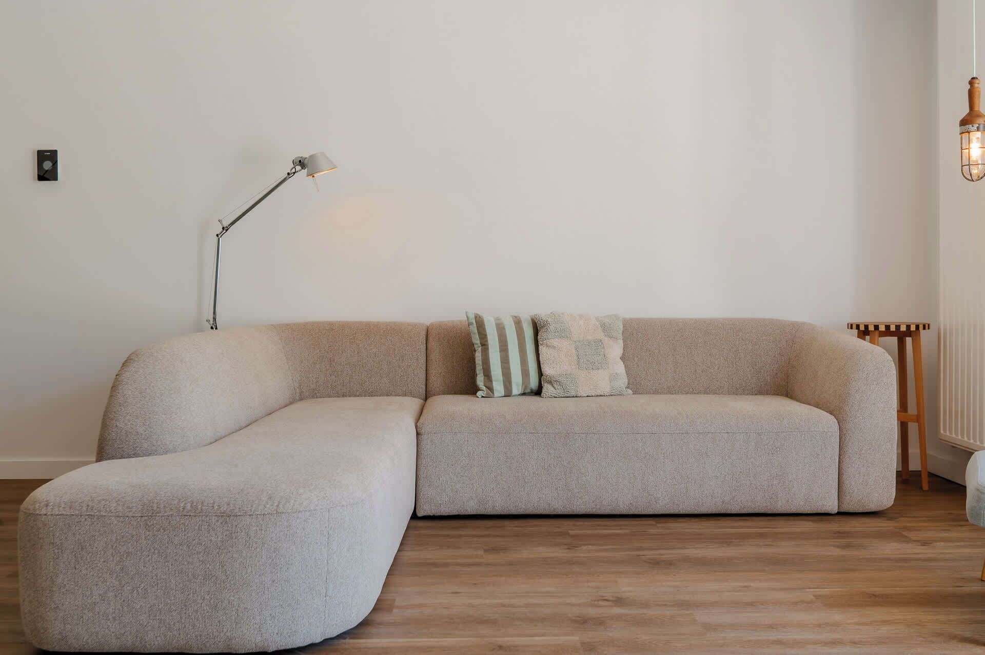 Un salon moderne avec un canapé d’angle, une lampe sur pied et une petite table d’appoint en bois.