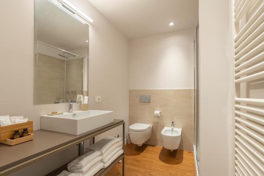 A modern bathroom with a large mirror, a sink, a toilet, and a bidet.