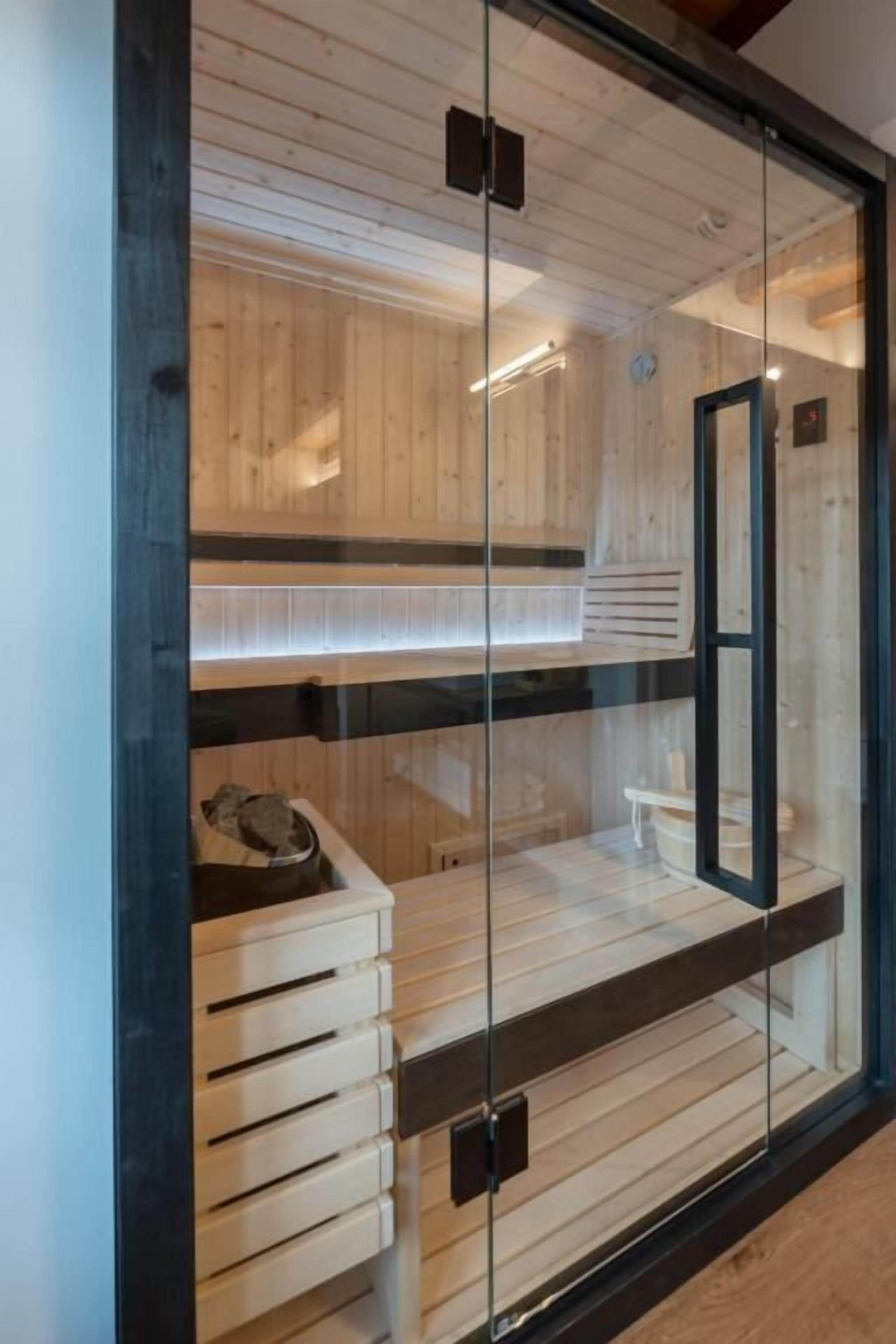 Un sauna doté de bancs en bois et d’une porte en verre, avec un design moderne et un plafond apparent.