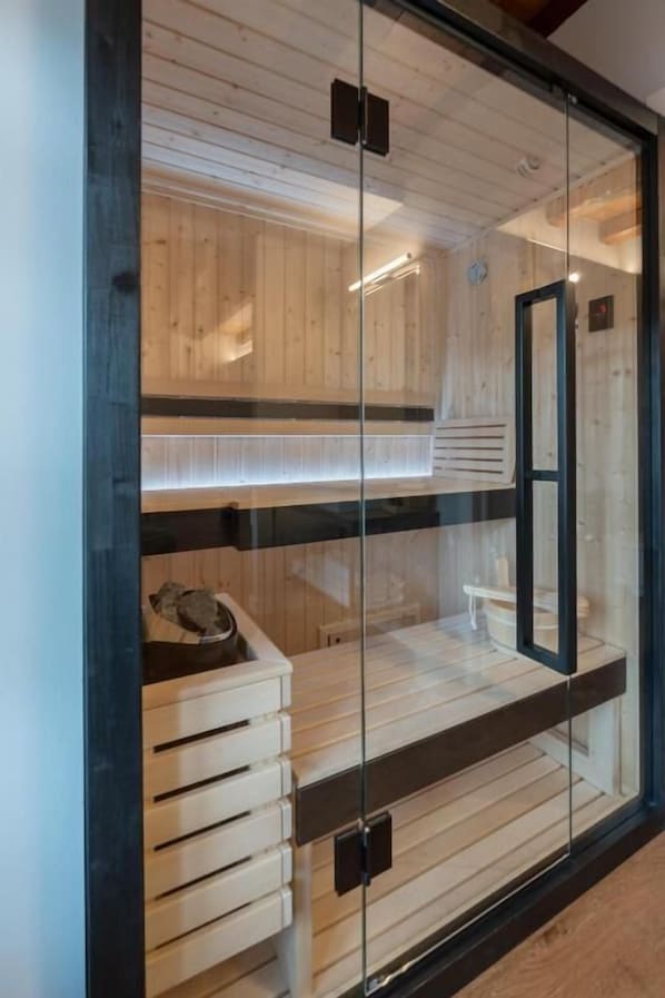 Una sauna con bancos de madera y puerta de vidrio, con un diseño moderno y techo visible.