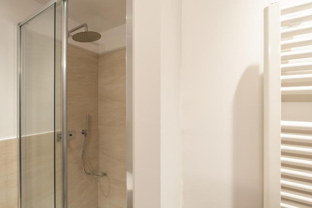 Une douche fermée par des parois en verre, dotée d’un pommeau de douche à main et d’un panneau de commande fixé au mur.