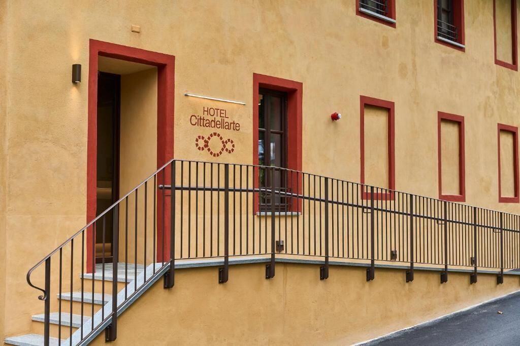 L’entrée d’un hôtel, avec un escalier et une enseigne indiquant le nom « HÔTEL Cittadellarte ».