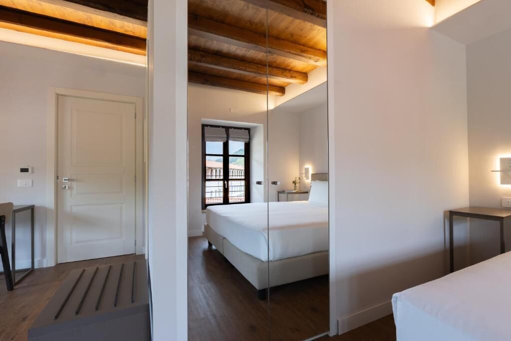Una camera d'albergo con un letto, comodini, una porta e una finestra con vista.