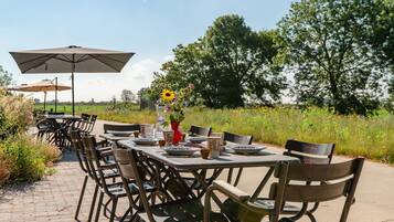 An outdoor dining area with tables and chairs, a large umbrella, and a vase with flowers.