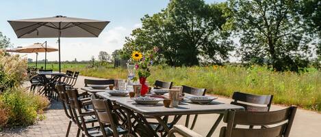 Un espace extérieur aménagé pour les repas, avec des tables et des chaises, un grand parasol et un vase rempli de fleurs.