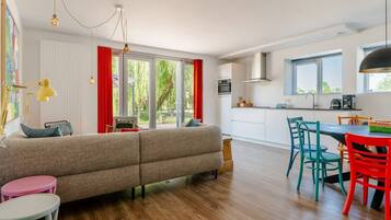A modern living room with a sofa, a dining table with chairs, and a kitchen area with a stove and cabinets.