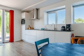 Ett modernt kök med en inbyggd ugn, en köksfläkt i rostfritt stål och en kaffebryggare på bänkskivan.