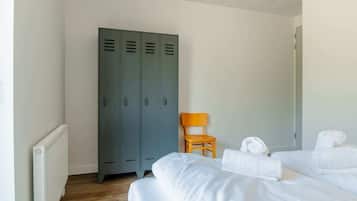 A hotel room with two beds, a wooden chair, and a set of grey lockers.