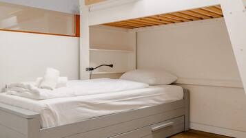 A bunk bed with a pull-out desk, white bedding, and a bedside lamp.