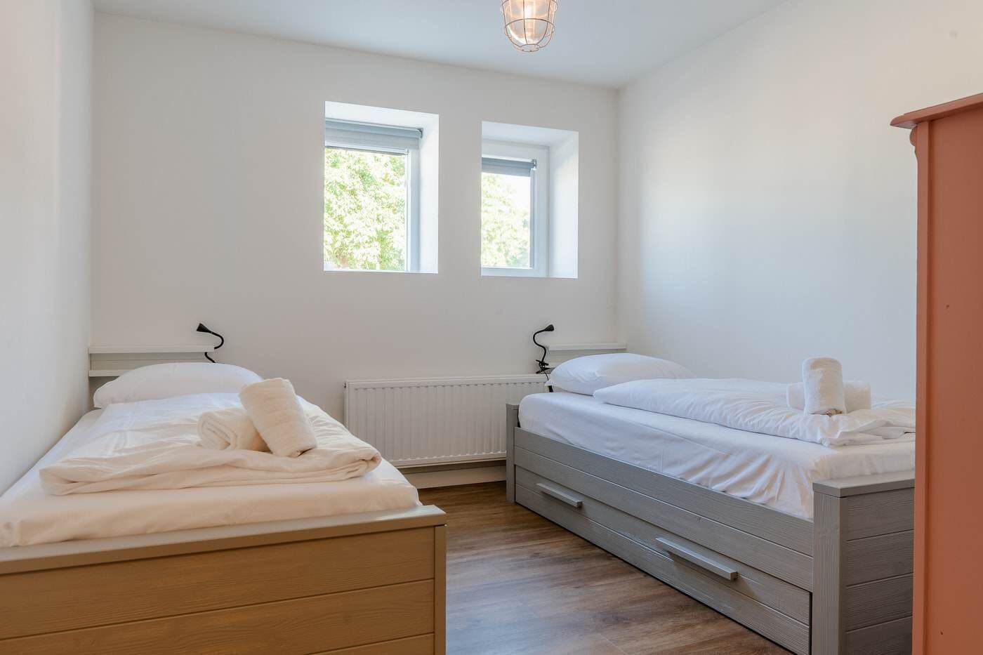 A bedroom with two beds, a radiator, and two windows.