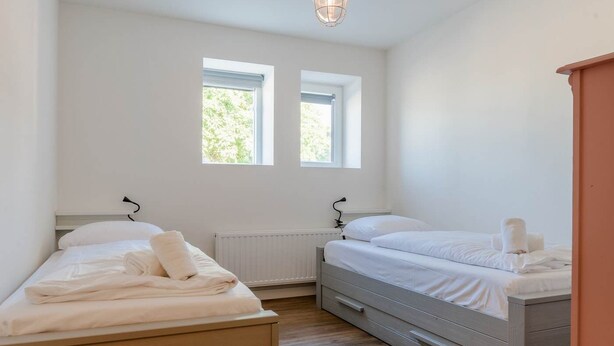 Un dormitorio con dos camas, un radiador y dos ventanas.