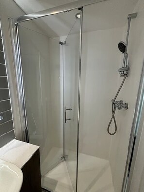 A glass-enclosed shower stall with a handheld showerhead and a wall-mounted faucet. - Student Only Bridle Works (Glasgow)