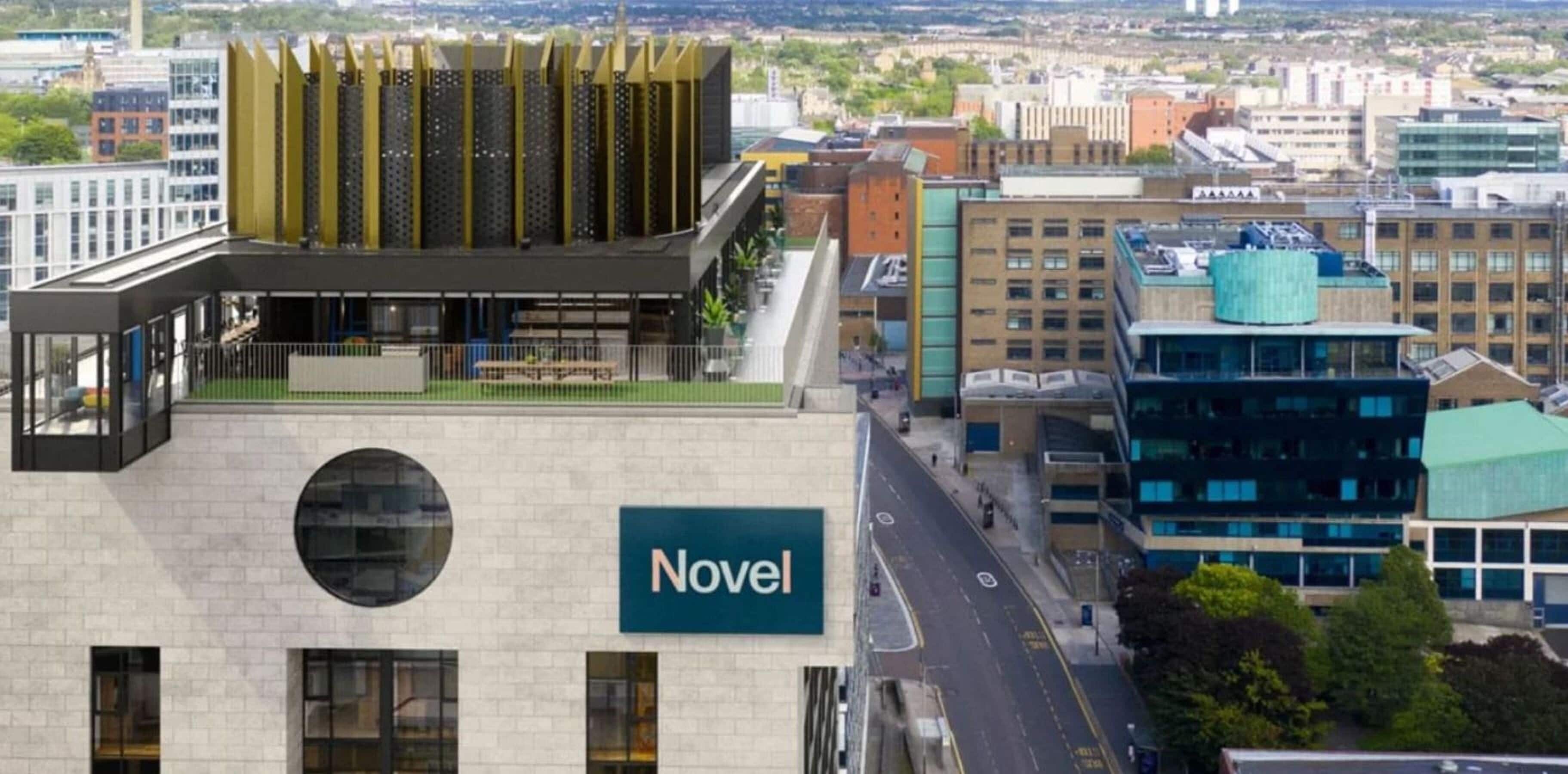 A modern building with a prominent 'Novel' sign, featuring a rooftop garden and a view of the cityscape.