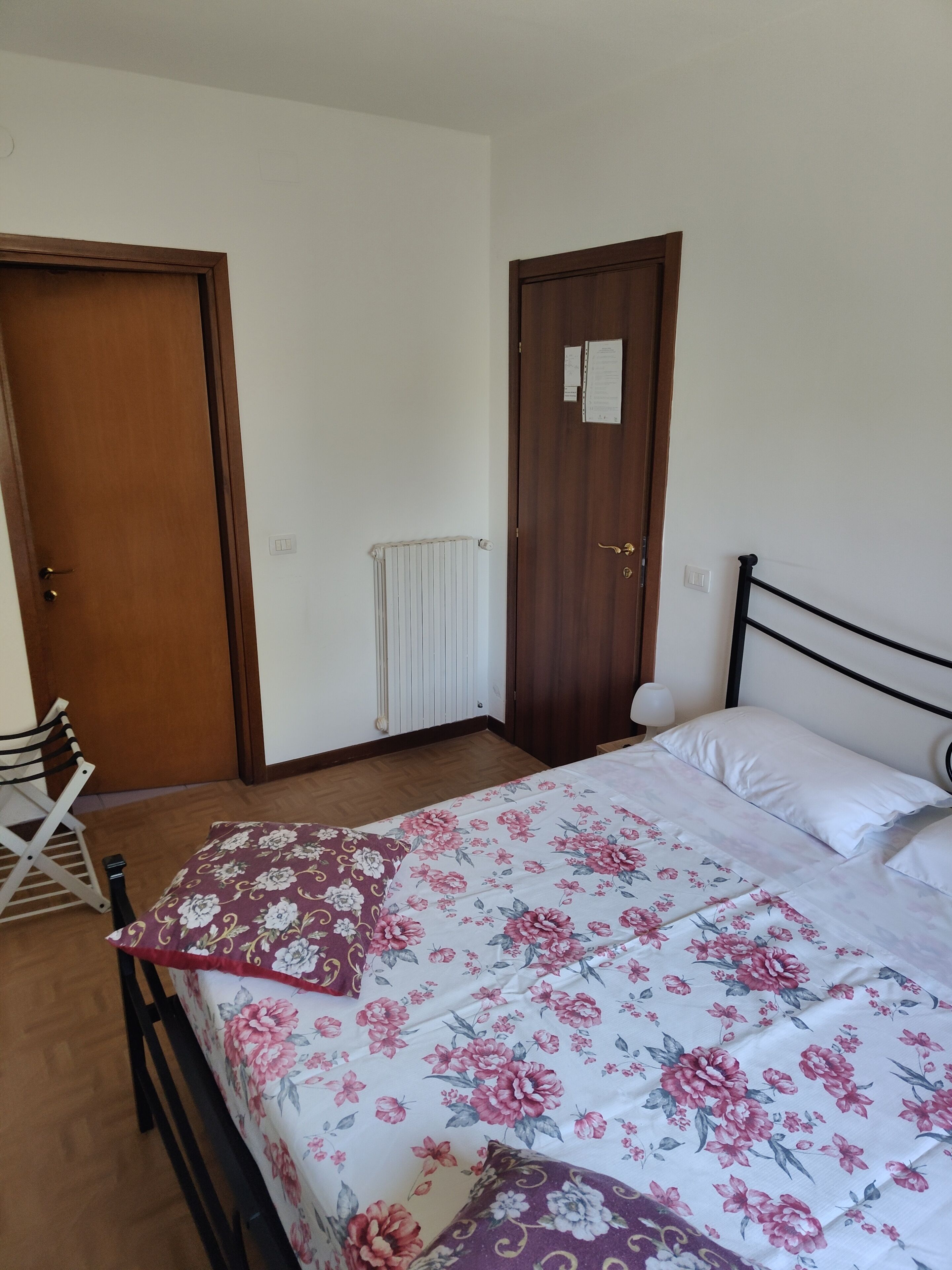 Ein Schlafzimmer mit Bett, Heizkörper, Holztür und Stuhl.