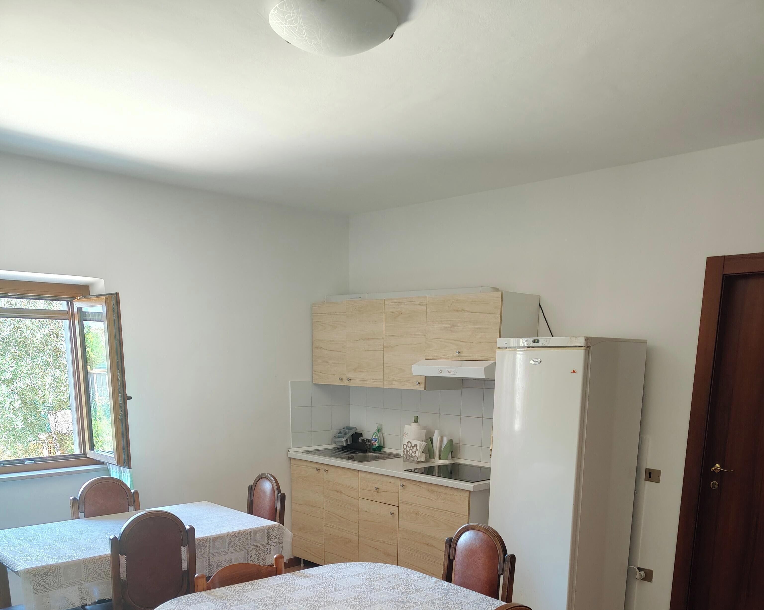 A compact kitchen with a dining table and chairs, a refrigerator, and a window providing natural light.