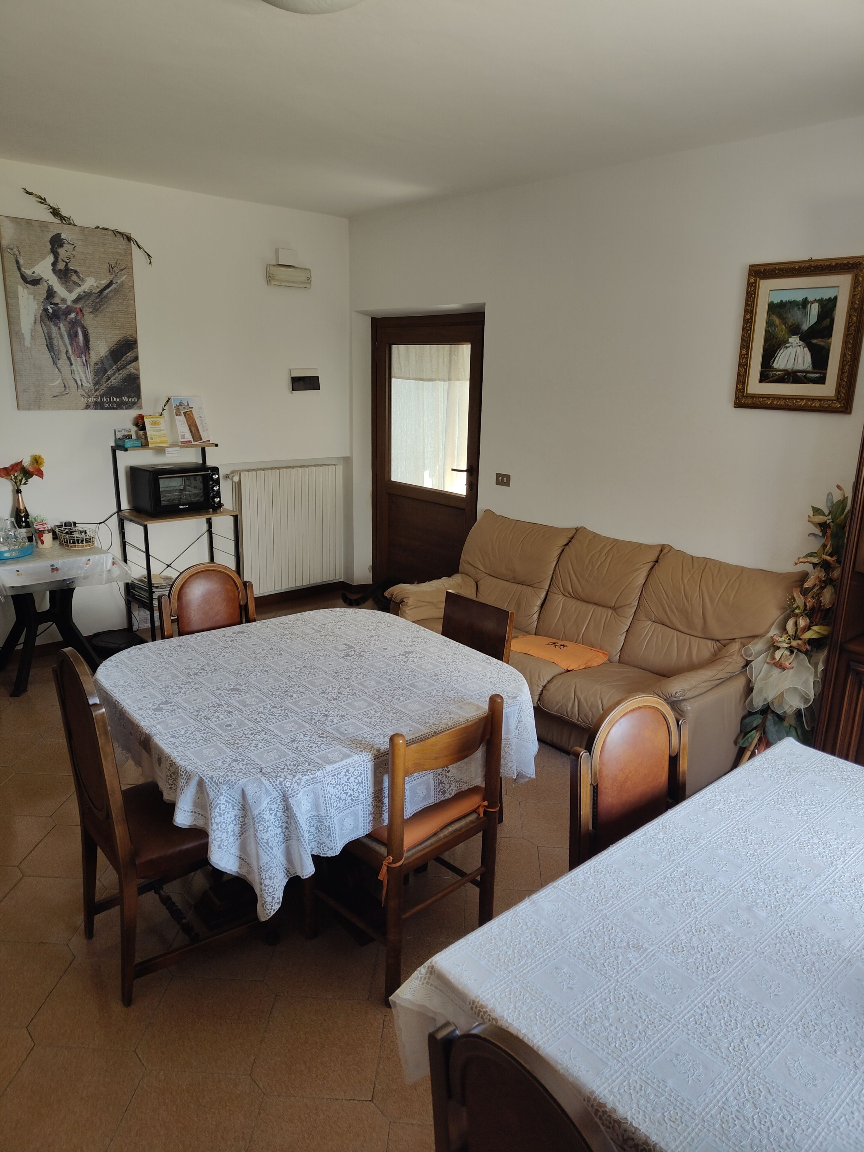 A dining area with a table and chairs, a sofa, a microwave, and a framed picture on the wall.