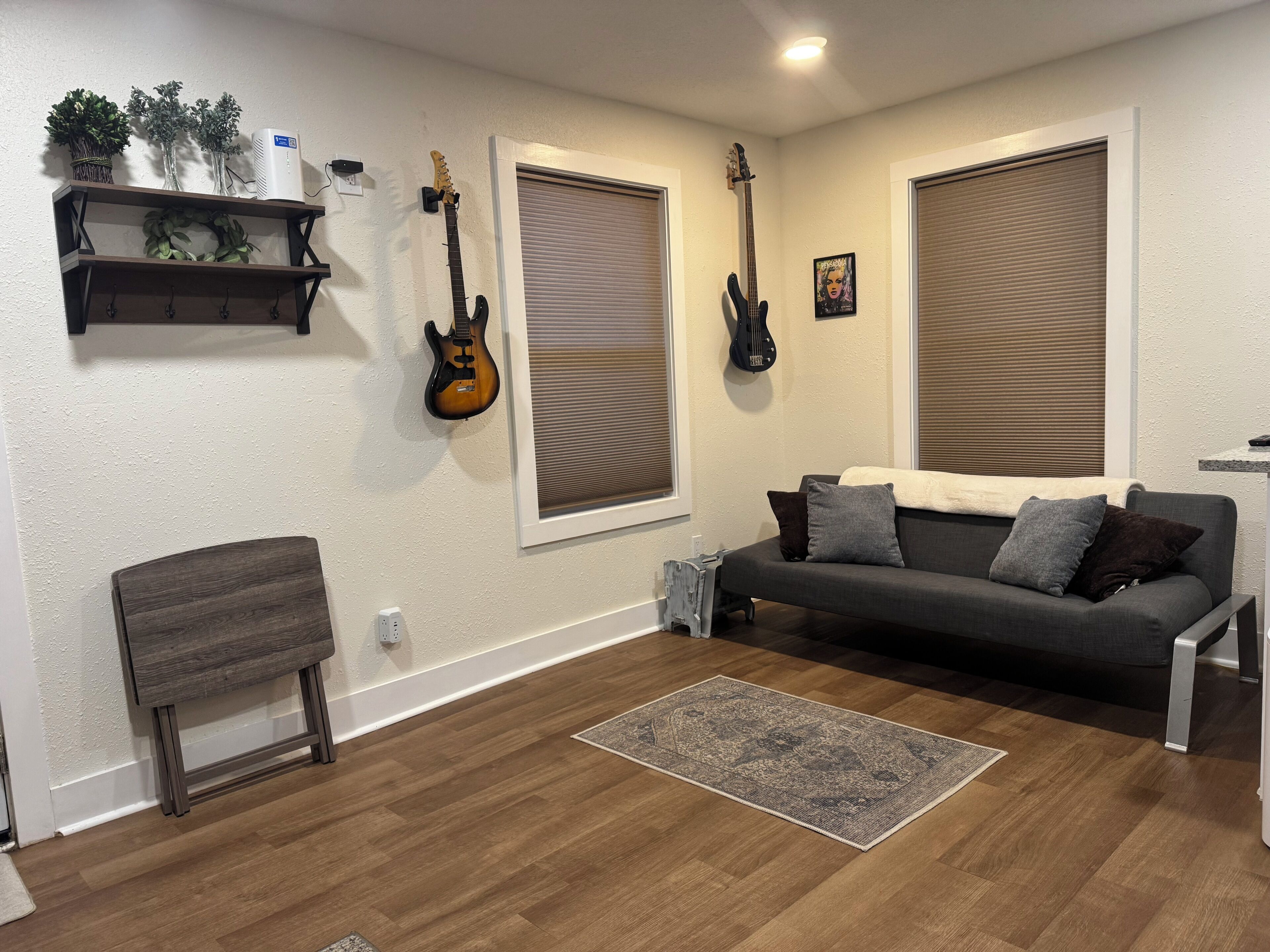 A living room with a grey sofa, two guitars on the wall, a small table, and a rug.