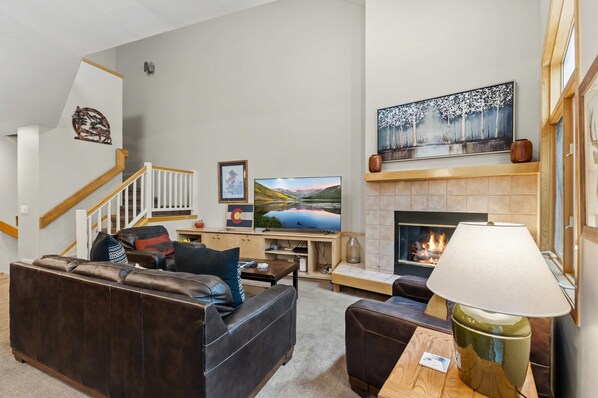 A living room with a fireplace, a television, and a staircase. - Breck Getaway | Walk to Slopes/Downtown + Hot Tub (Breckenridge)