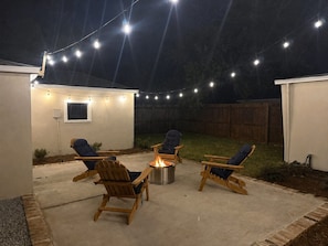 Une terrasse extérieure avec des chaises en bois et un foyer, le tout agrémenté de guirlandes lumineuses.