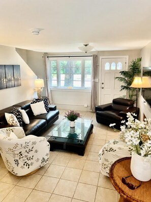 A living room with a sofa, armchair, and coffee table, a door with a window, and a ceiling fan. - Cozy 2-bedroom house in beautiful Bay St. Louis with AC (Bay St. Louis)