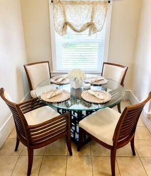 A round glass table with four wooden chairs, each with a cushion. A floral centerpiece is on the table. - Cozy 2-bedroom house in beautiful Bay St. Louis with AC (Bay St. Louis)