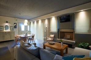Una sala de estar moderna con sofá, mesa de comedor, sillas, chimenea y televisor montado en la pared.