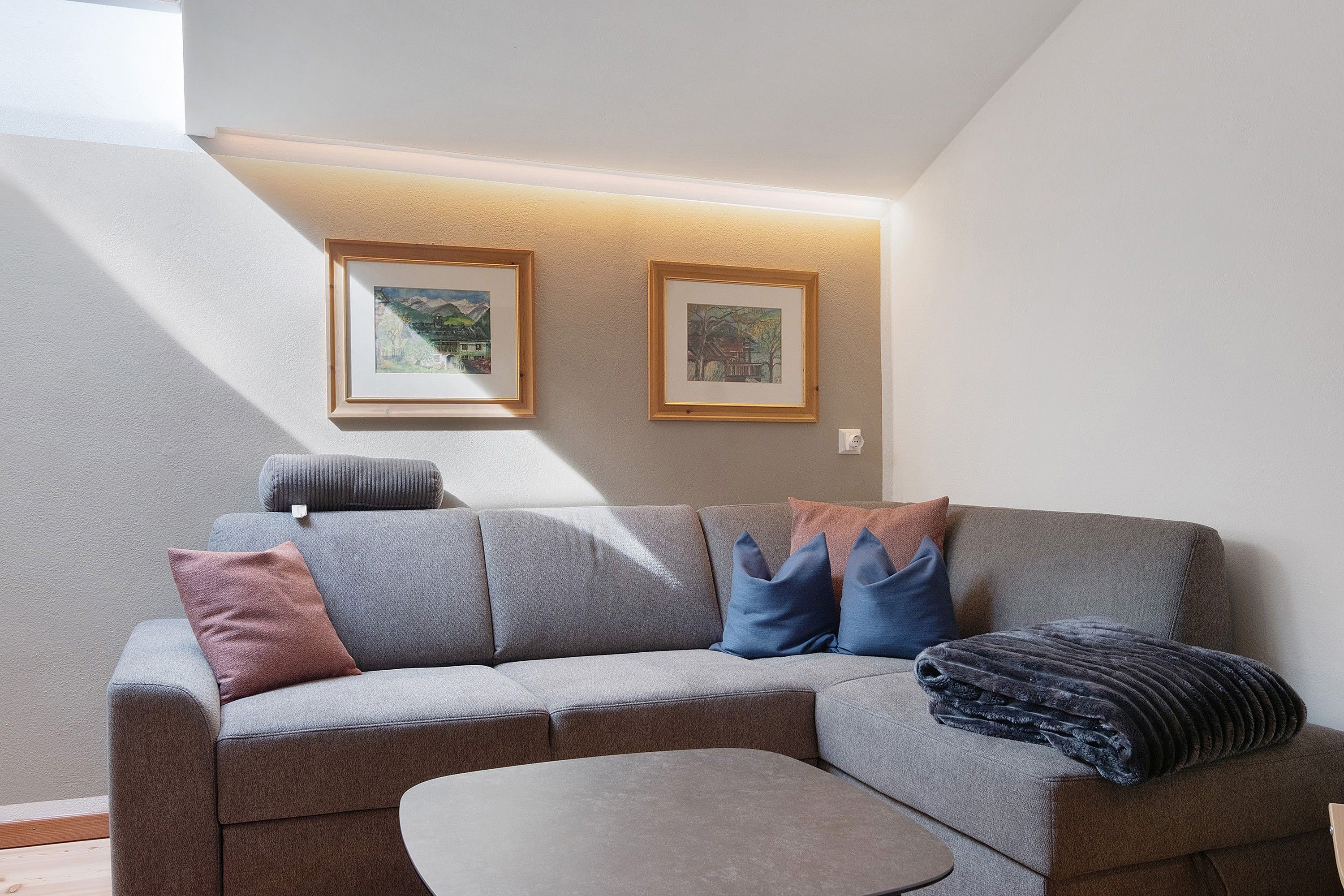 A modern living room with a grey sofa, a small coffee table, and two framed artworks on the wall.