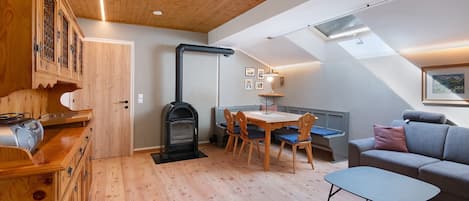 Une pièce chaleureuse avec un plafond en bois, un poêle encastré, une table à manger avec des chaises, un canapé et une petite table.