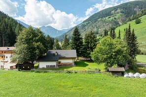 Una casa amb teulada inclinada, envoltada per un jardí ben cuidat i arbres, amb muntanyes al fons.