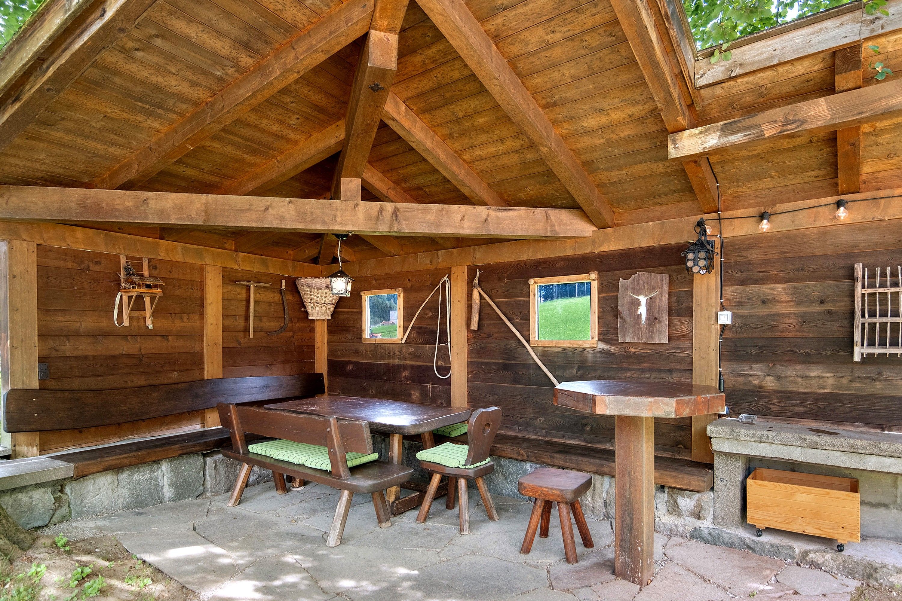 A rustic wooden cabin with a dining area featuring a table and benches, a stone fireplace, and a view through a window.