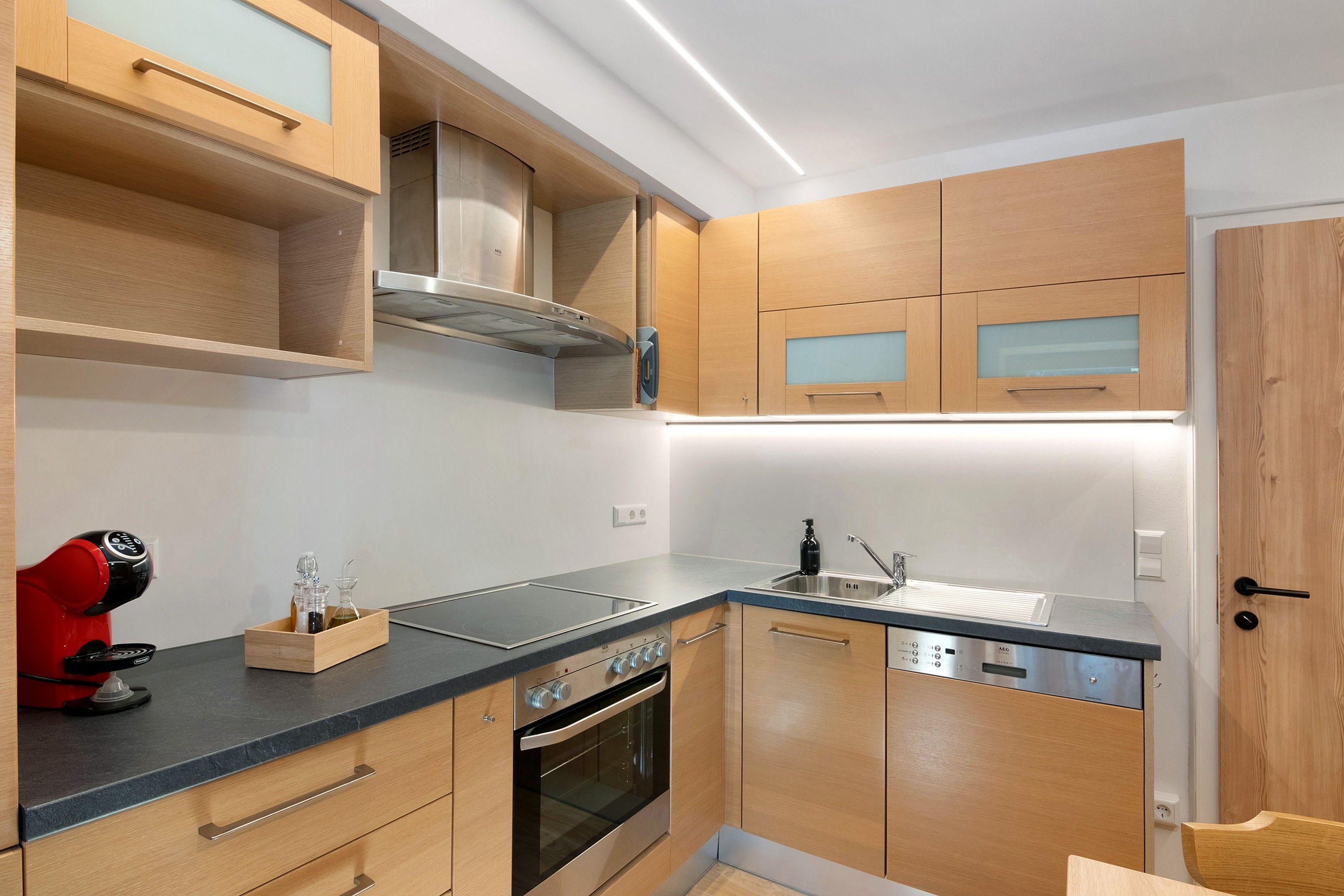 A modern kitchen with wooden cabinets, a built-in oven, a stainless steel range hood, and a black countertop.