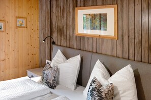 Quarto com parede de madeira, quadro emoldurado, luminária de cabeceira e almofadas estampadas.