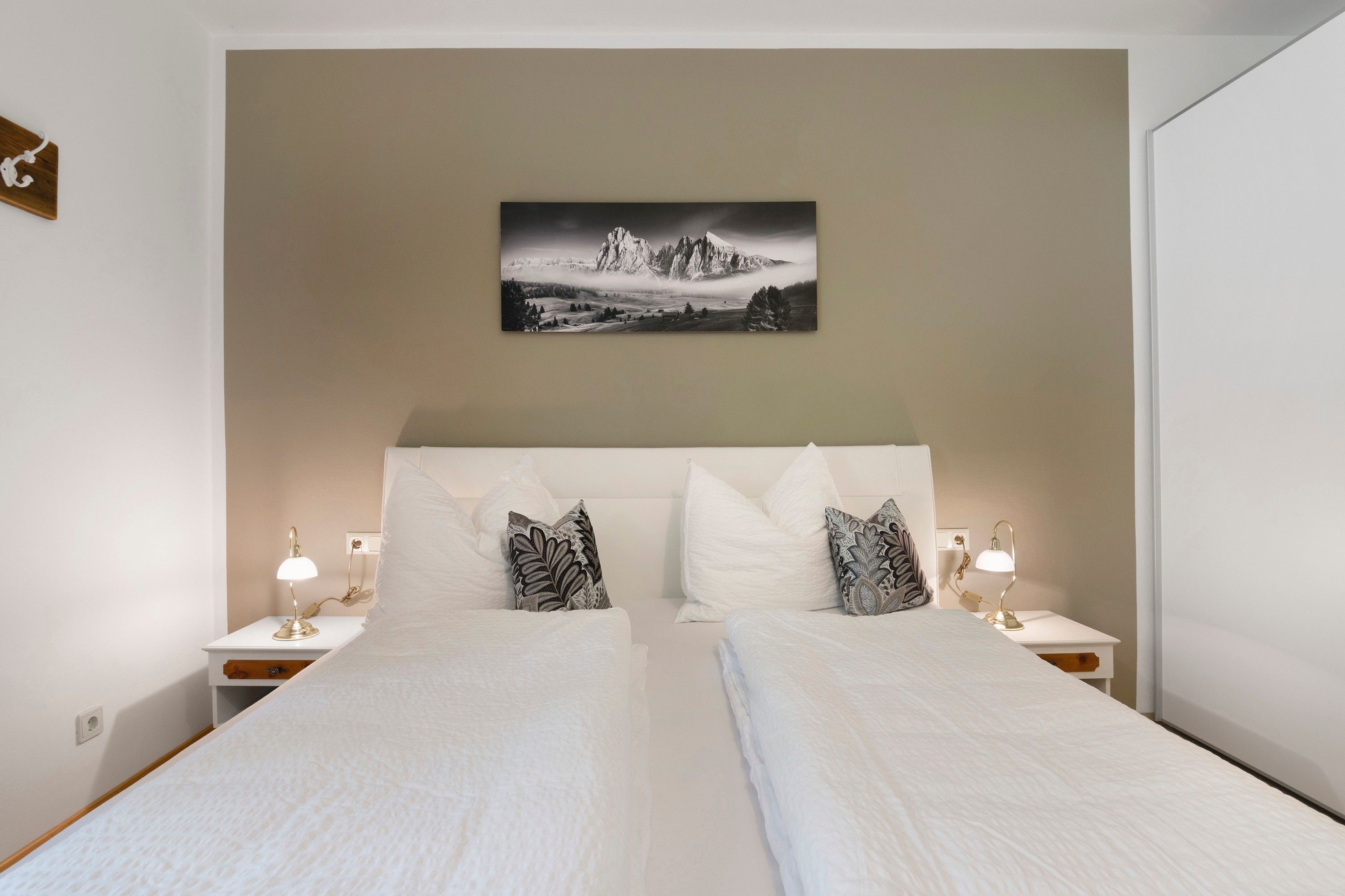 A double bed with white bedding, two nightstands with lamps, and a wall-mounted picture of a mountain landscape.