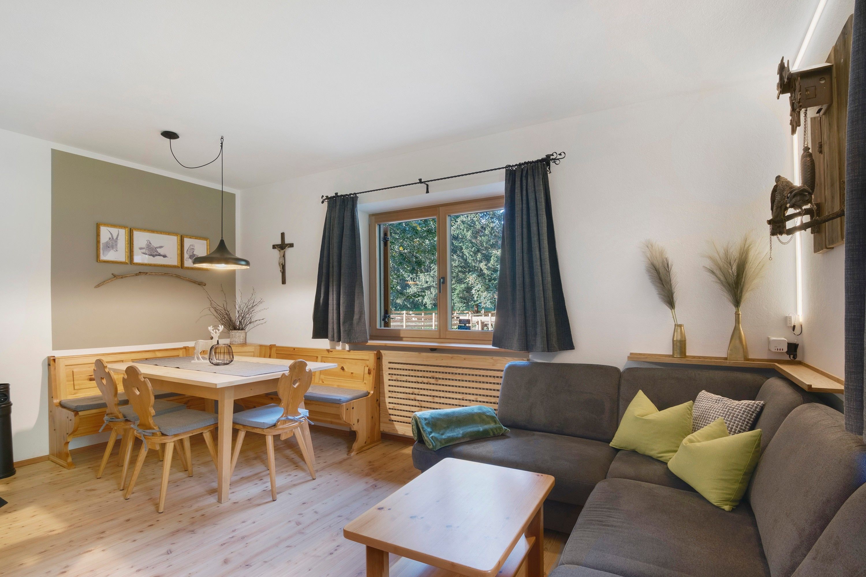 A cozy living room with a wooden dining table, chairs, a sofa, and a window with curtains.