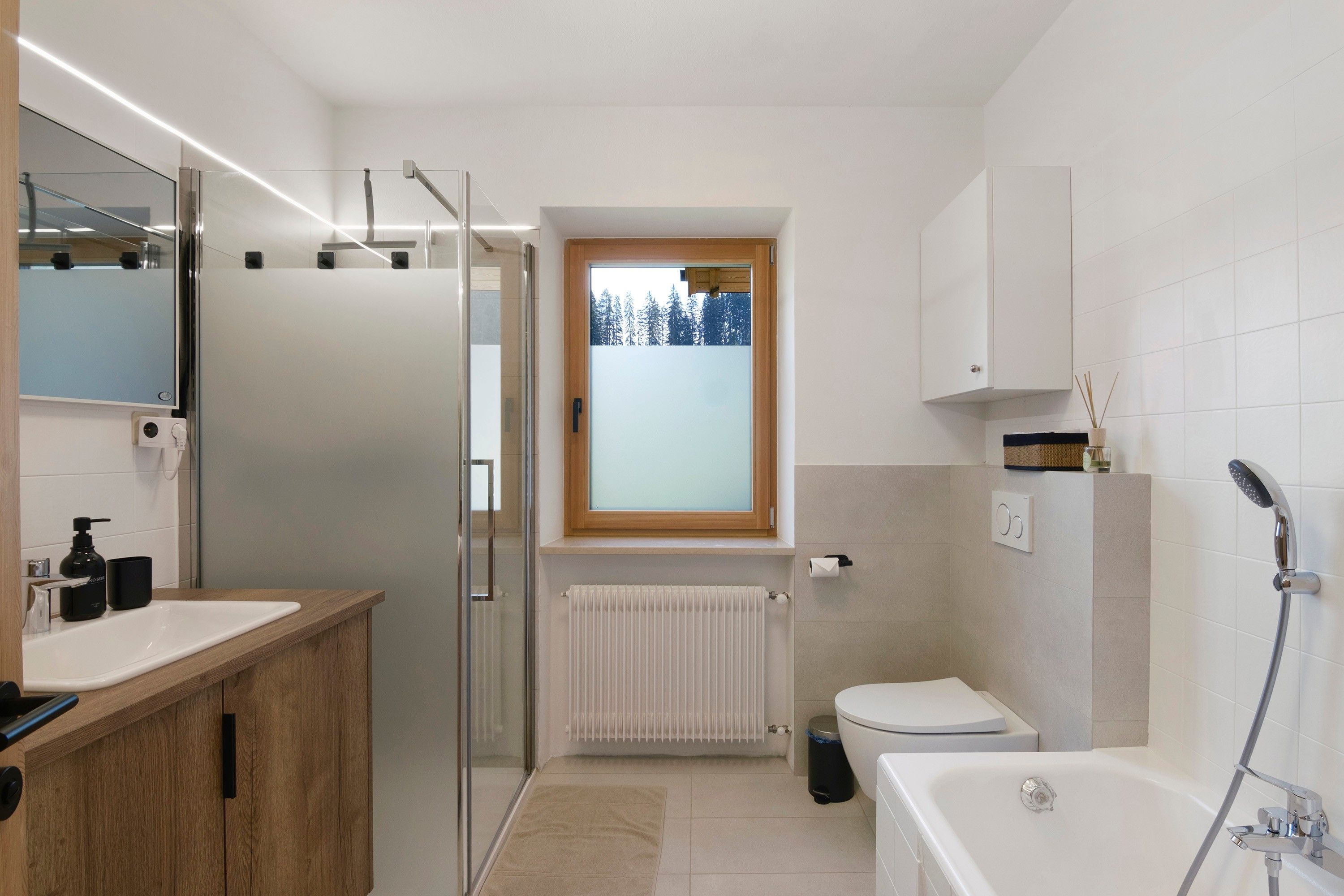 Ein modernes Badezimmer mit Duschkabine aus Glas, Toilette, Badewanne und Waschtisch mit Spiegel.