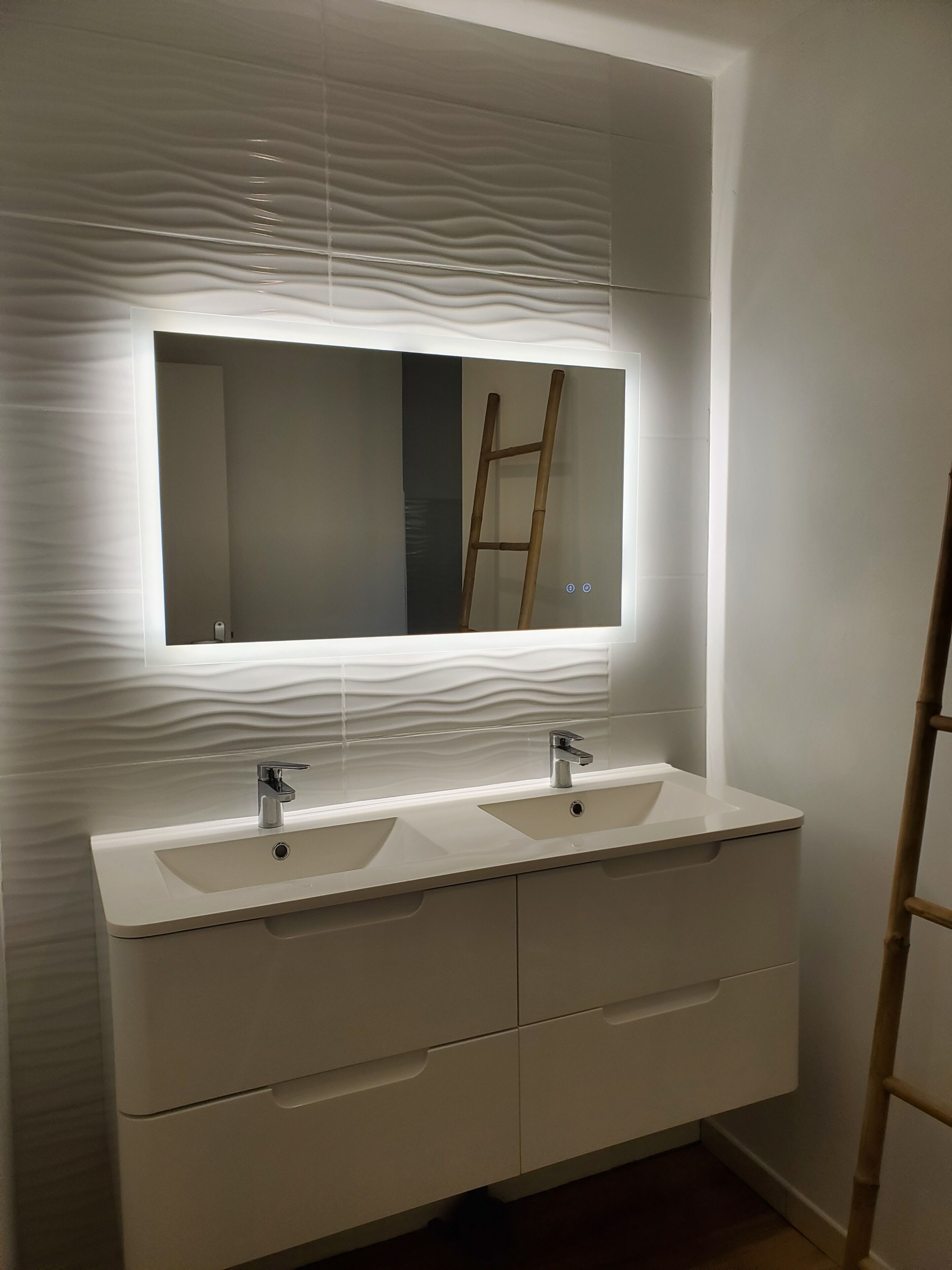 A bathroom with a white vanity, two sinks, a mirror, and a wooden ladder leaning against the wall.