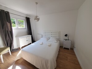 A bedroom with a bed, a bedside table, a lamp, a window, and a radiator. - A house between the ocean, the Basque Country, and Spain. 5 minutes from the beach (LABENNE)