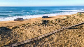 Una playa con un paseo marítimo de madera, dunas de arena y el océano al fondo.