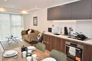 A modern living room with a sofa, a dining table set for four, and a kitchen area with appliances and utensils. - Bright and Spacious 1 Bed Apartment in Leeds (Leeds)