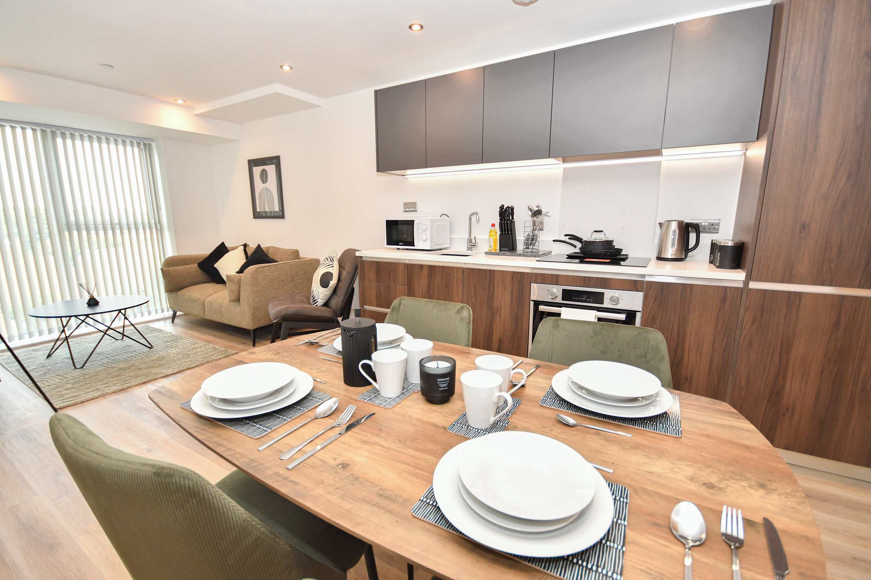A modern kitchen with built-in appliances, a dining area with a wooden table set for four, and a living room with a sofa and a coffee table.