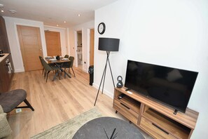 A modern living room with a flat-screen TV, a dining area with chairs and a table, and a hallway leading to a bathroom. - Bright and Spacious 1 Bed Apartment in Leeds (Leeds)