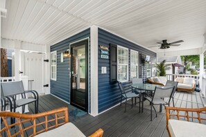 A covered outdoor area with a dining table and chairs, a small seating area with a sofa, and a door leading to a building with a 'WELCOME' sign.