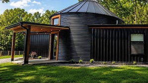 A modern, black metal building with a circular roof, a covered porch, and a small window.