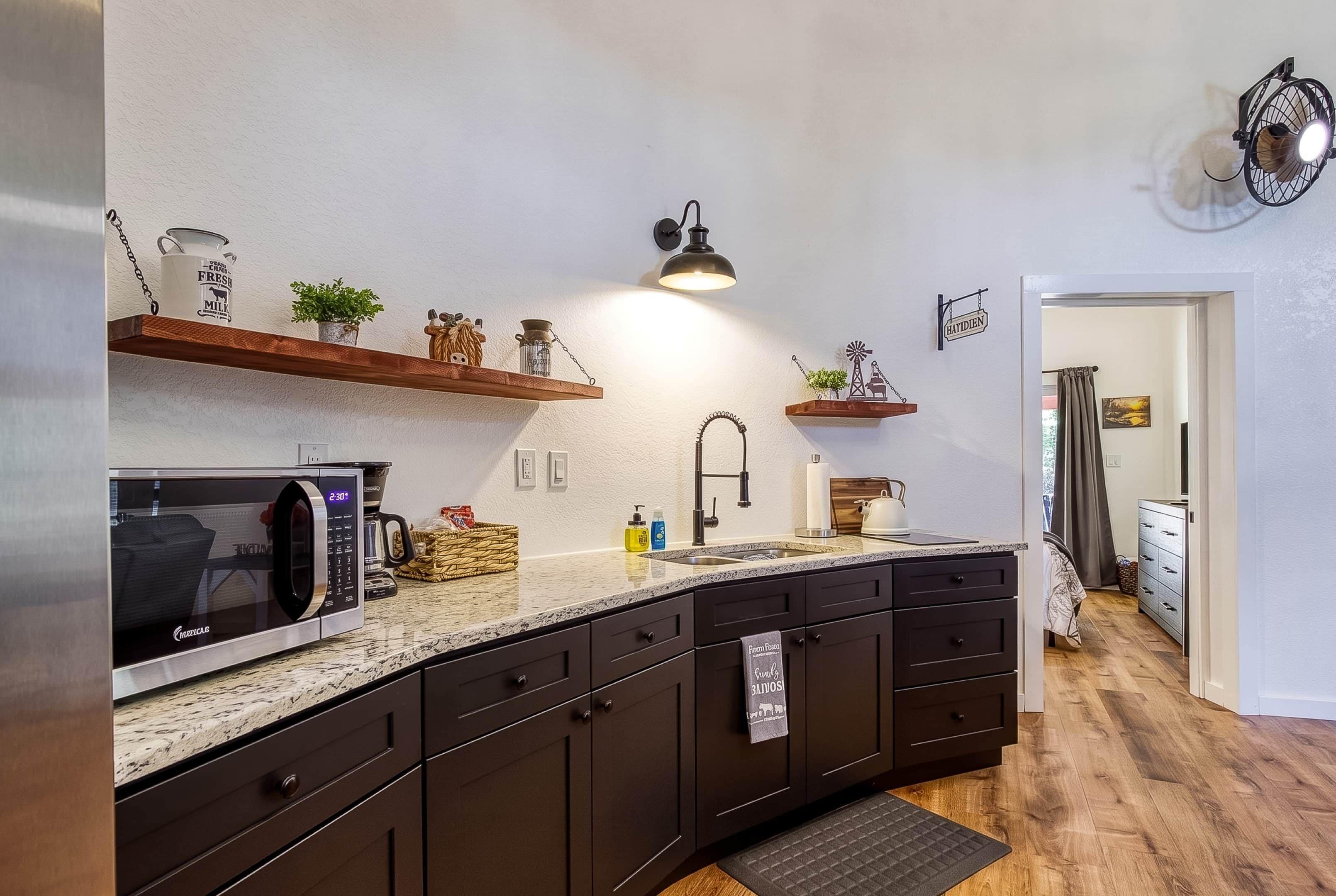 A modern kitchen with dark cabinetry, a granite countertop, a built-in microwave, and a hanging light fixture.