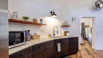 A modern kitchen with dark cabinetry, a granite countertop, a built-in microwave, and a hanging light fixture.