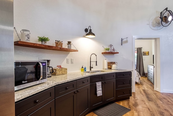 A modern kitchen with dark cabinetry, a granite countertop, a built-in microwave, and a hanging light fixture.